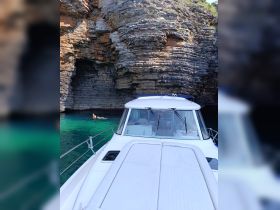 A scenic view of a boat anchored near a rocky coastline, with a swimmer enjoying the clear turquoise waters — a perfect spot for exploration and relaxation.