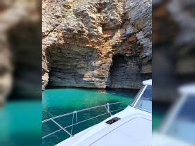 A swimmer enjoys the stunning turquoise waters near a rocky cave, with a boat providing the perfect vantage point for this picturesque scene.