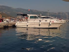 A sleek yacht docked at the marina, showcasing its elegant design against a scenic backdrop of mountains and clear waters.