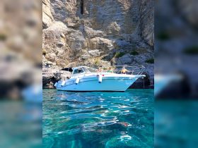A group enjoys a sunny day on a boat anchored in crystal clear waters, surrounded by stunning cliffs — perfect for relaxation and fun on the water.