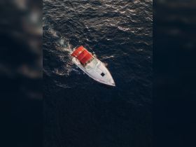 Aerial view of a sleek speedboat cruising through deep blue waters, showcasing the vessel's elegant design and vibrant red canopy.