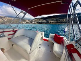 A cozy interior view of a boat's seating area, featuring plush cushions and a scenic backdrop of the water and shoreline, perfect for relaxing during a day on the water.