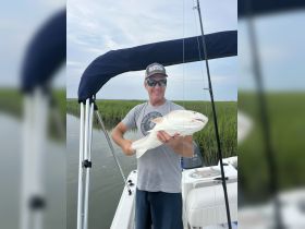 A proud angler holds up his catch while fishing from a boat, showcasing the excitement of a successful day on the water.
