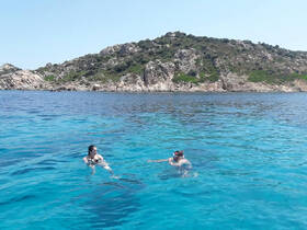 Two friends enjoy a refreshing swim in crystal-clear waters, surrounded by stunning island scenery — a perfect moment for adventure seekers.