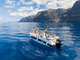 A joyful group celebrates on a boat in the ocean, surrounded by stunning cliffs and clear blue waters — perfect for unforgettable adventures at sea.
