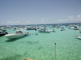 A vibrant scene at a popular sandbar, filled with boats and groups of people enjoying swimming and relaxing in the clear turquoise waters.