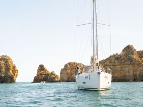 A picturesque view of a sailboat navigating through calm waters, framed by stunning rocky cliffs — an ideal scene for sailing enthusiasts and coastal adventures.