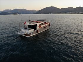 A stunning aerial view of a sleek yacht cruising through calm waters, set against a backdrop of mountains and a serene coastline.