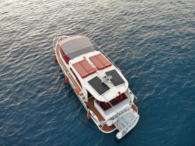 Aerial view of a sleek yacht cruising over calm waters, showcasing its elegant design and solar panels — perfect for eco-friendly boating adventures.