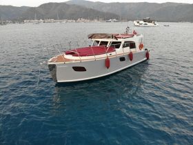A stunning view of the 'BARBAROS 3' yacht anchored in calm waters, showcasing its elegant design against a picturesque backdrop of mountains and a marina.