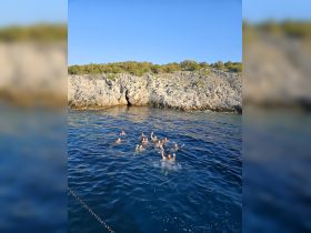 A lively group enjoys swimming in the clear waters near a rocky coastline, capturing the essence of summer fun and adventure on the water.