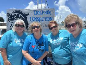 A cheerful group of friends celebrates their girls trip at Dolphin Connection, showcasing their matching shirts and smiles against a vibrant backdrop.