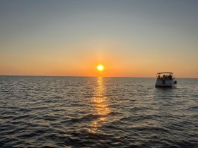 A picturesque sunset over the water with a boat in the foreground, creating a serene atmosphere perfect for evening cruises.