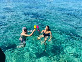 A couple enjoys a refreshing toast in the crystal-clear waters, celebrating their day with colorful cocktails — a perfect moment for fun and relaxation on the water.