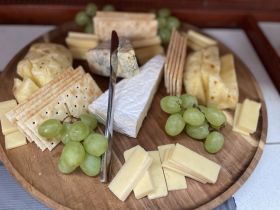 A beautifully arranged charcuterie board featuring an assortment of cheeses, crackers, and fresh grapes, perfect for onboard snacking during a boat trip.