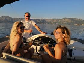 A joyful group enjoys cocktails on the deck of a boat, surrounded by stunning mountain views — perfect for sunset cruises and celebrations on the water.