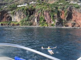 A swimmer enjoys the clear waters near a stunning rocky coastline, showcasing the beauty of the landscape and the joy of on-water activities.