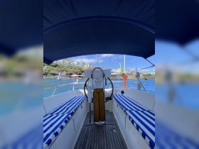 Interior view of a boat's helm and seating area, featuring comfortable striped cushions and a scenic backdrop of the coastline.