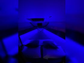 A cozy cabin interior illuminated with blue lighting, featuring comfortable bedding and pillows, perfect for relaxing on a boat.