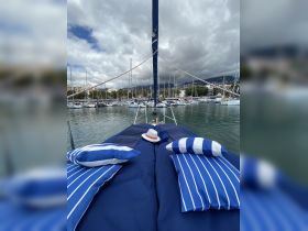 A cozy seating area on a sailboat, featuring blue and white striped cushions and a sun hat, perfect for relaxing while enjoying the marina views.