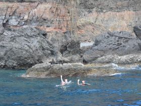 Two snorkelers enjoy swimming in clear waters near a rocky coastline, showcasing the beauty of underwater adventures.