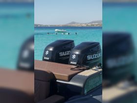 Close-up of Suzuki outboard engines on a boat, with swimmers enjoying the clear turquoise waters in the background, showcasing the perfect setting for water activities.