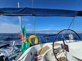 A view of the helm and interior of a sailing boat, showcasing the steering console and nautical decor against a backdrop of open water and distant land.