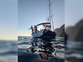 Two friends joyfully jump from the side of a yacht into the water, capturing the essence of summer fun and adventure on a sunset cruise.