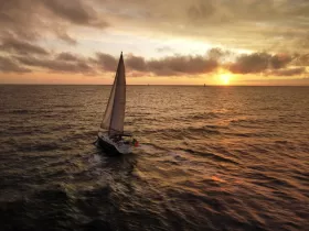 A stunning aerial view of a sailboat gracefully navigating the ocean at sunset, showcasing the beauty of sailing against a vibrant sky.