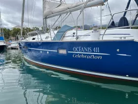A close-up view of the Océanis 411 named 'Celebration' docked in calm waters, showcasing its sleek design and vibrant blue hull.