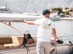 A crew member prepares the boat while guests relax onboard, showcasing a perfect day on the water with stunning views in the background.