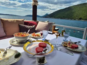 A beautifully set table featuring a delicious spread of food and drinks, perfect for enjoying a meal on the water with stunning views of the coastline.