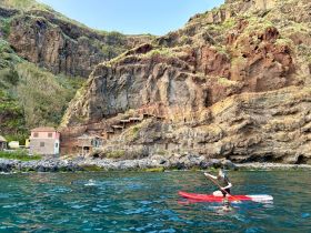 A kayaker paddles along a stunning coastline, with a snorkeler exploring the clear waters nearby — a perfect adventure for nature lovers.