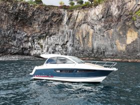 A sleek Leader yacht cruising along a rocky coastline, showcasing its elegant design against a stunning natural backdrop.