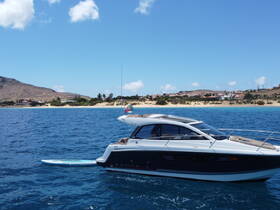 A sleek yacht glides through clear blue waters, showcasing its elegant design against a picturesque coastal backdrop.