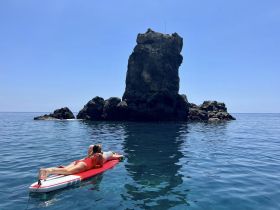 A person enjoys paddleboarding in crystal-clear waters near a striking rock formation, capturing the essence of a perfect day on the water.