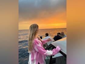A young woman enjoys a stunning sunset aboard a boat, surrounded by friends — a perfect moment for celebration on the water.