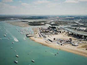 A stunning aerial view of a vibrant harbor with numerous boats and a sandy beach, showcasing the beauty of coastal landscapes and recreational activities.