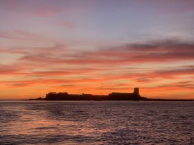 A breathtaking sunset casts vibrant colors over the coastline, creating a picturesque backdrop for evening boat trips.
