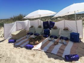 A beautifully arranged beach setup featuring umbrellas, towels, and a cooler filled with snacks, perfect for a relaxing day by the shore.