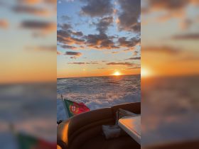 A stunning sunset view from a boat with the Portuguese flag waving, capturing the serene beauty of the ocean waves and the vibrant colors of the sky.