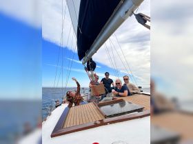 A lively group enjoys a sailing adventure, capturing joyful moments on deck with drinks and smiles against a beautiful sky.