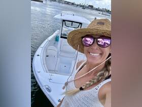 A smiling woman takes a selfie on a boat, showcasing the beautiful water and marina in the background — perfect for capturing memorable moments on the water.