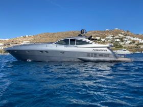 A sleek Pershing 54 yacht glides through the vibrant blue waters, showcasing its elegant design against a picturesque coastal backdrop.