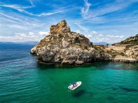 A stunning aerial view of a boat navigating through crystal-clear waters near a rocky coastline, showcasing the beauty of the marine landscape.
