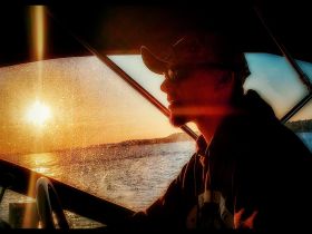 A silhouette of a captain enjoying a sunset while steering the boat, capturing the essence of a serene evening on the water.