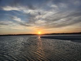 A stunning sunset over tranquil waters, showcasing the beautiful coastline — perfect for capturing the essence of serene boating experiences.
