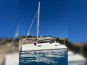 A stunning side view of a catamaran sailing in clear waters, showcasing its sleek design against a backdrop of rocky cliffs and a bright blue sky.