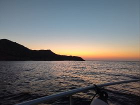 A serene sunset view from a boat, showcasing the tranquil waters and silhouetted coastline — perfect for evening cruises.