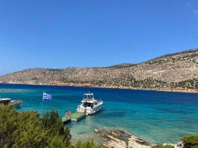 A picturesque view of a boat docked at a stunning beach in Greece, with guests enjoying the sun and clear turquoise waters — an ideal destination for summer adventures.
